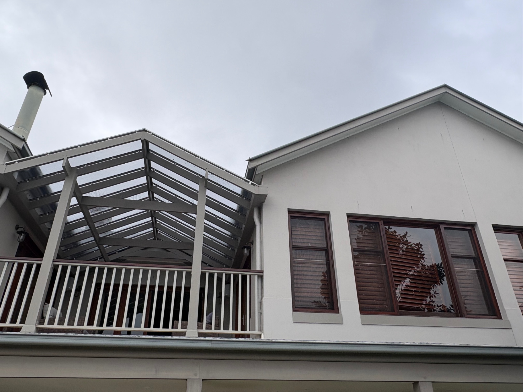 Glass-roofed pergola over the upper balcony beside timber-framed windows